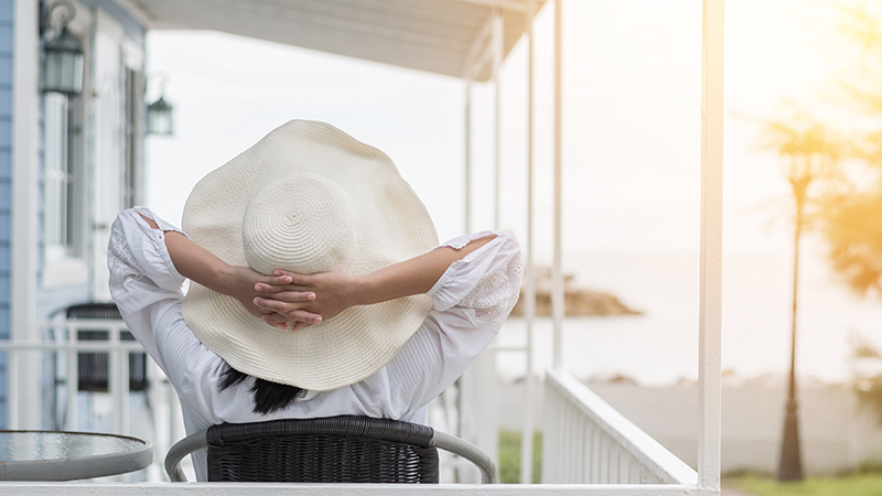 Young girl lifestyle wearing summer hat on sunny day relaxing taking it easy happily sitting on porch at beach-house on beach front enjoying healthy living life quality for holiday vacation concept